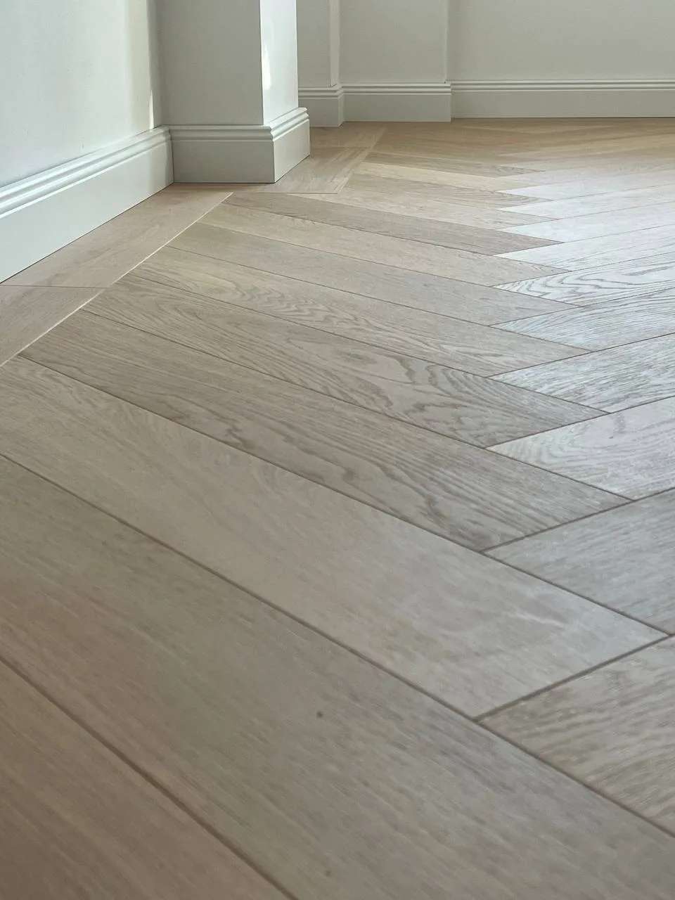 Detailaufnahme von neu verlegtem Fischgrät-Parkett an einer weißen Sockelleiste